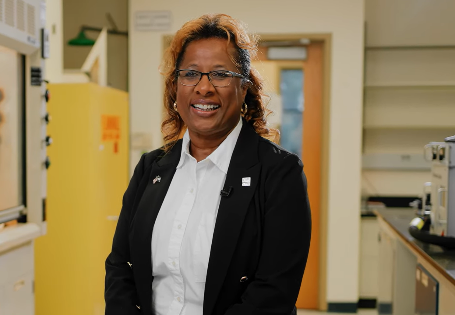 Dr. Deidra R. Hodges standing in her research laboratory, wearing a black blazer and white shirt